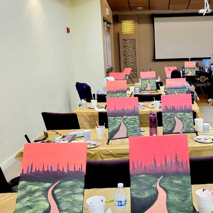 Room with tables set up for a painting activity, featuring art supplies and canvas boards.